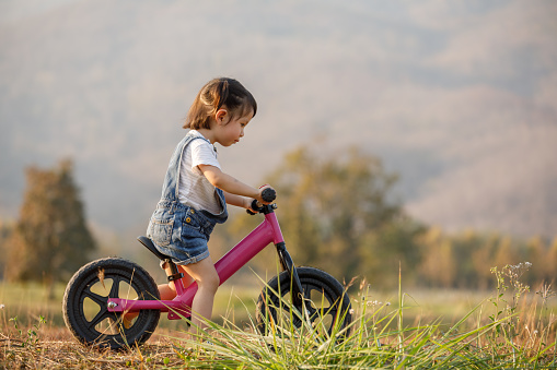 Happy child riding a bike. Little girl on a pink bicycle. Healthy preschool children summer activity. Kids playing outside. Little girl learns 
to keep balance while riding a bicycle