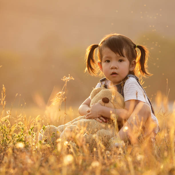 adorável garotinha de 3 anos brincando com ursinho de pelúcia ao ar livre em um dia muito ensolarado.  ao pôr do sol com sinalizador - preschool 2 3 years preschooler little girls - fotografias e filmes do acervo