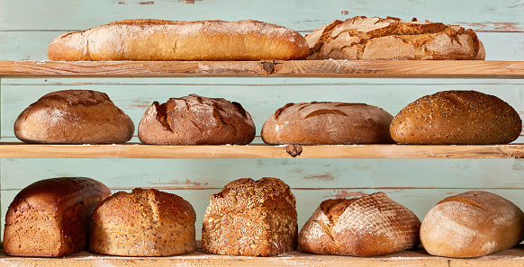 Abundance of different types of freshly baked bread loaves placed on shelves against worn out wooden background in light studio