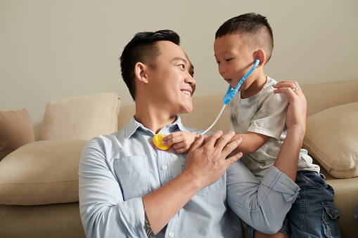 Little kid listening to heartbeat of his dad with toy stethescope