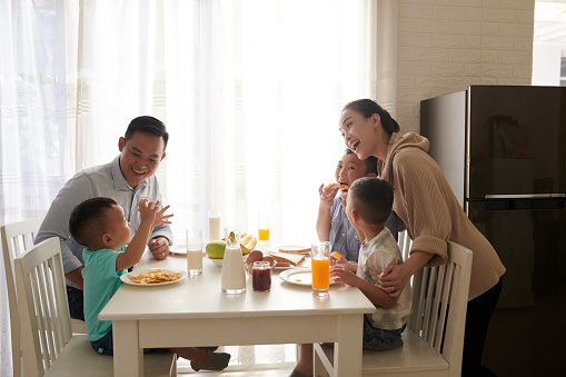 Happy joyful Asian family of five eating tasty breakfast at kitchen table