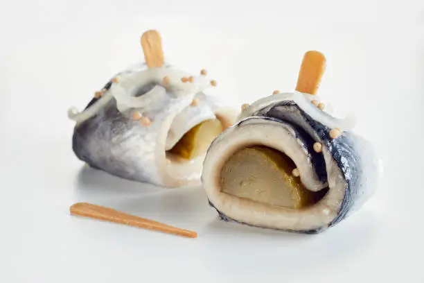 Closeup of delectable rollmops made of herring fillet and pickled cucumbers with onions served on white table