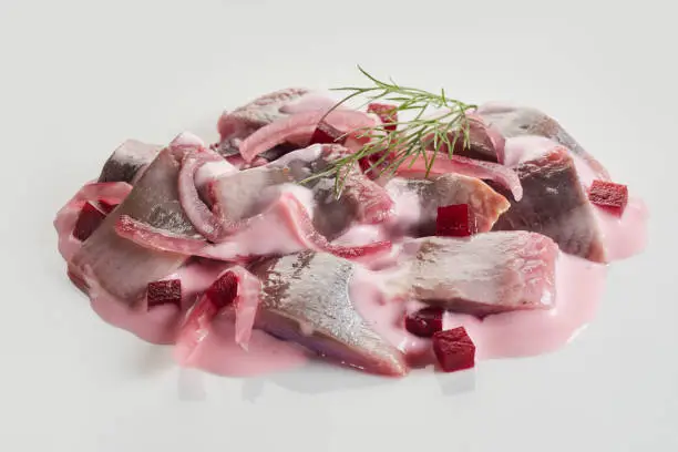 High angle closeup of appetizing salad from fresh beetroot and herring fish garnished with dill and served on white background