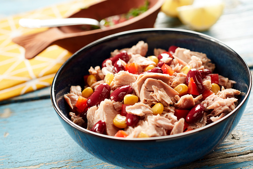 High angle of appetizing salad with tuna fish and canned beans and corn in bowl placed on wooden table