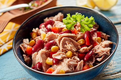 High angle closeup of bowl with appetizing tuna salad with canned beans and corn served on wooden table