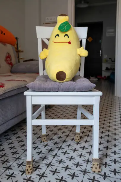 Photo of plush toy pillow banana on the white chair, creative interior design