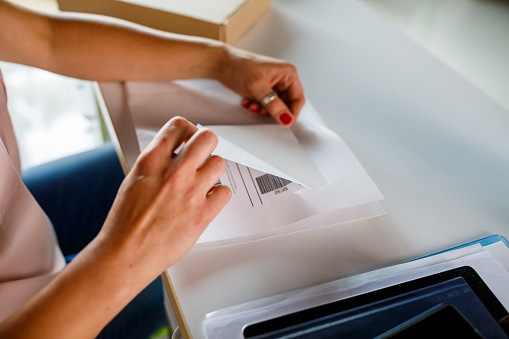 Close up shot of unrecognizable woman sitting at her desk and peeling off the label she is about to stick on a package she is preparing for shipping.