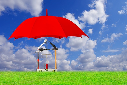 Tool House protected by red umbrella in meadow against blue sky,
Insurance and real estate concept.