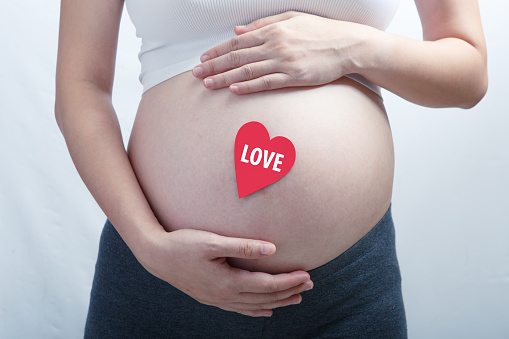 Pregnant woman with single pink heart on her baby bump. All on white background.