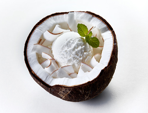From above of cold ice cream scoop decorated with mint leaf served in coconut shell on white background