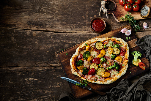 From above of tasty vegetarian pizza with various vegetables served on wooden cutting board on table in kitchen