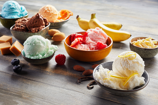 From above of bowls with assorted colorful scoops of ice cream served on wooden table