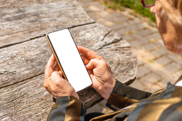 istock Senior woman hands using smartphone empty white screen mockup while sitting at old wooden table background. Technology and copy space for advertising concept. 1405544095