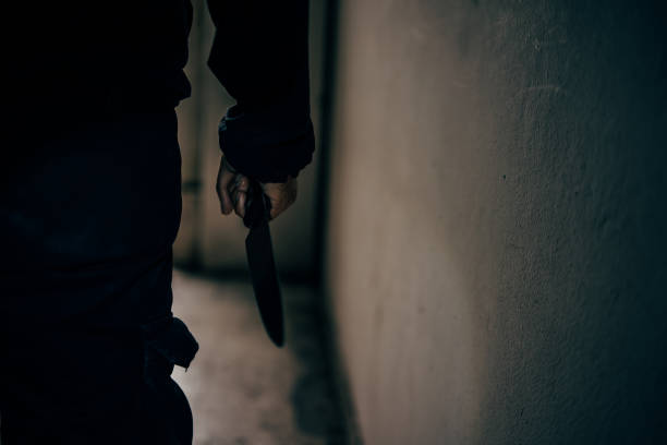 vista trasera de un asesino sosteniendo un cuchillo en una aterradora habitación oscura está a punto de atacar a la víctima. - mass murder fotografías e imágenes de stock