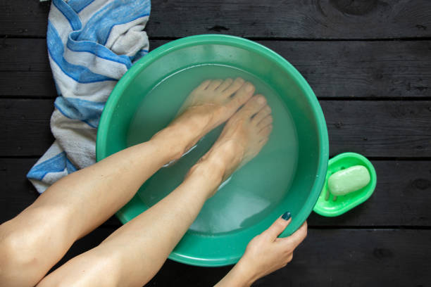 ragazza lava i piedi in una ciotola d'acqua sul pavimento di legno a casa, cura dei piedi, lavare i piedi a casa - treated water foto e immagini stock