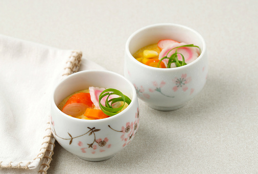 Pot Steamed Hotchpotch Japanese Chawan Mushi on Cream Background with Narutomaki, Carrot, Corn, Crabstick, and Green Onion Topping