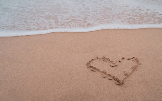 Heart symbol of love hand drawn on sand summer beach background.