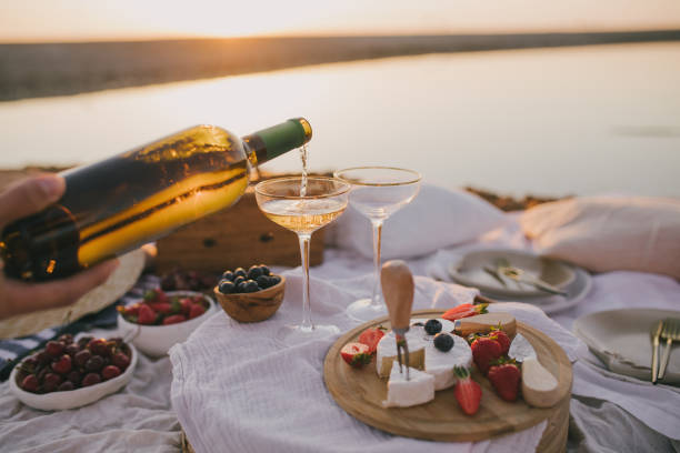 piękny romantyczny piknik z dwoma kieliszkami białego wina, świeżego sera i jagód na plaży o zachodzie słońca. - couple dinner summer sunlight zdjęcia i obrazy z banku zdjęć