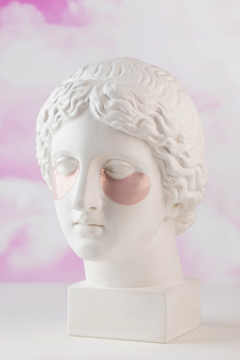 Hydrogel pink patches on the plaster head of Aphrodite on a pink background close-up. Beauty concept.