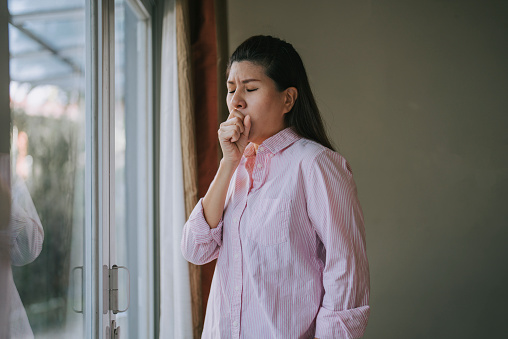 Asian Chinese woman coughing at home beside window