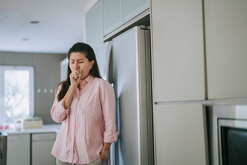 Asian Chinese woman coughing in kitchen feeling unwell