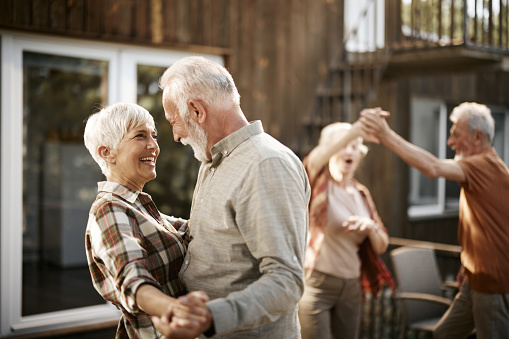 Happy mature couple and their friends enjoying in dancing during a party on a patio.