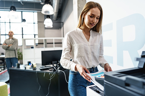 Young employee using modern printer in office, close up