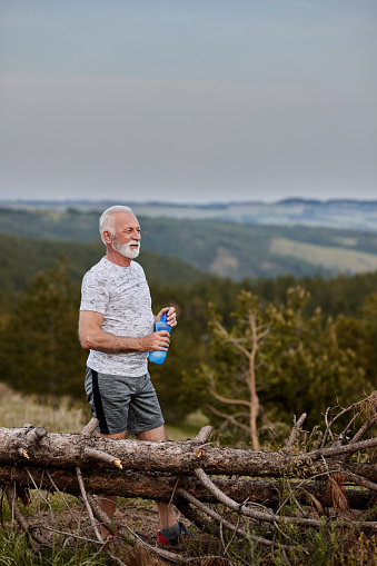 Mature male athlete resting on water break from sports training on a mountain. Copy space.