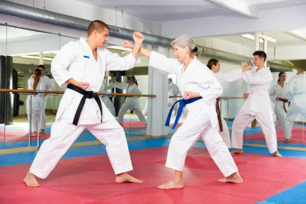 Portrait of concentrated aged woman wearing white kimono sparring with male opponent during martial arts training in gym