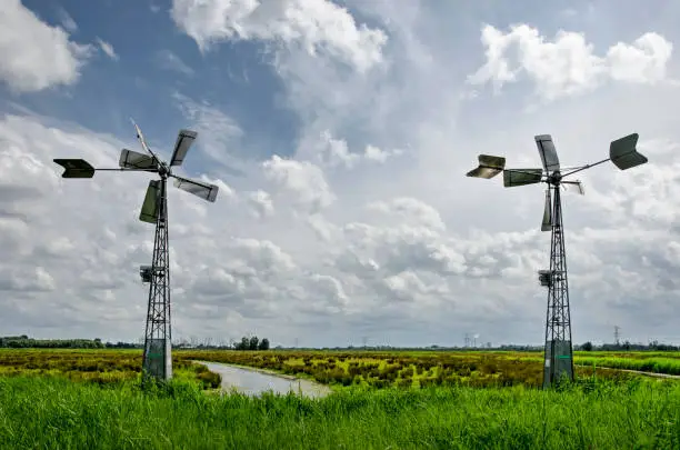 Two small modern windmills in a landscape with swamps and meadows under a sky with scattered clouds in the Noordwaard region in Biesbosch national park