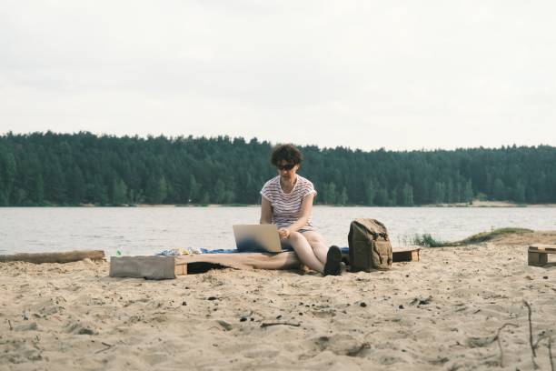 istock Woman is working at laptop while resting on forest lakeshore 1405562576