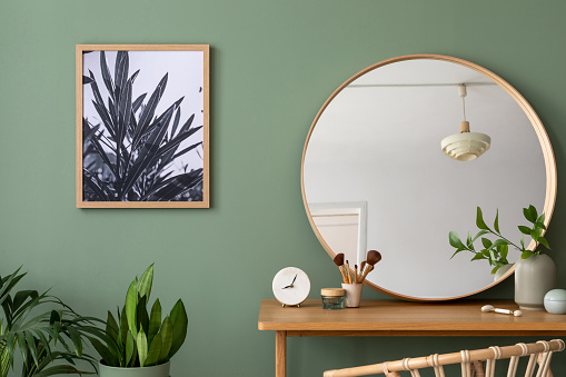 Elegant details of modern interior design with poster, round mirror, plant and stylish personal accessories. Wooden vanity table. Mock up poster. Template.