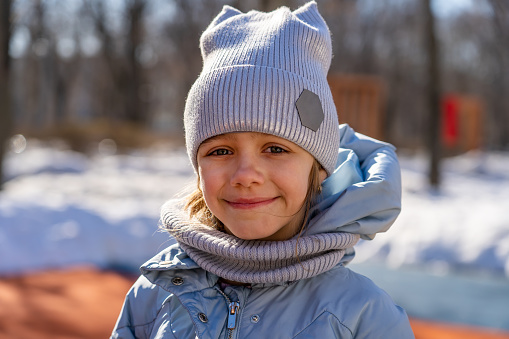 Portrait of little girl in blue jacket and knitted hat in snowy spring park