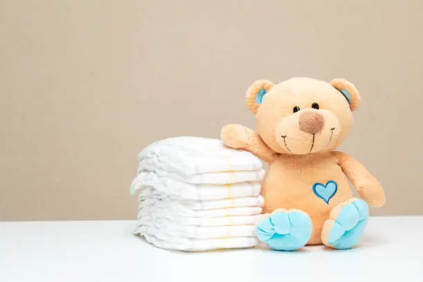 Photo of Stack of diapers with toy teddy bear on table. set for boy girl for baby shower with copy space