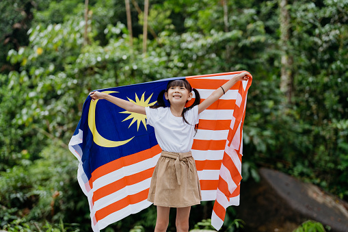 Image of a young Malaysian Chinese girl waving Malaysian flag and celebrating Malaysia Independence Day or Hari Merdeka