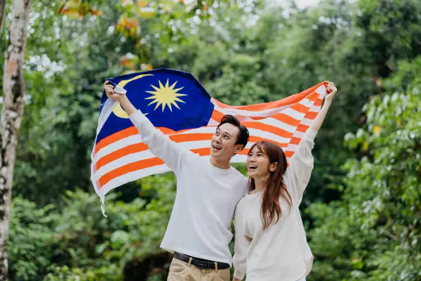 Image of a Malaysian Chinese couple waving Malaysian flag and celebrating Malaysia Independence Day or Hari Merdeka