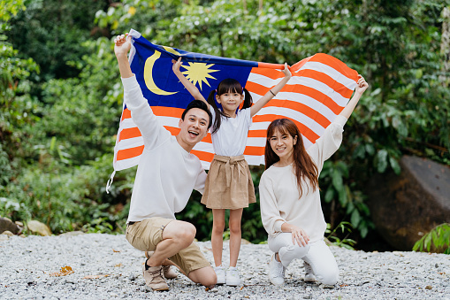 Image of a Malaysian Chinese family waving Malaysian flag and celebrating Malaysia Independence Day or Hari Merdeka