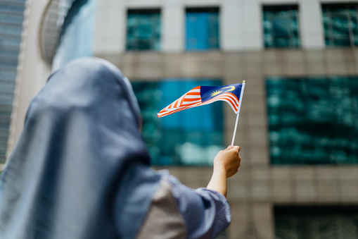 Image of a young Malaysian Malay woman waving Malaysian flag and celebrating Malaysia Independence Day or Hari Merdeka