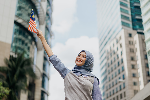 Image of a young Malaysian Malay woman waving Malaysian flag and celebrating Malaysia Independence Day or Hari Merdeka