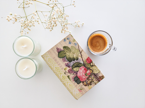 coffee cup, white candles and floral book on white background with flowers
