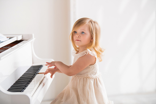 A little baby plays a big white piano in a bright sunny room