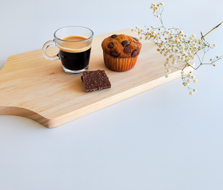 cup of coffee, vanilla muffin and chocolate on wooden board with white flowers on white background