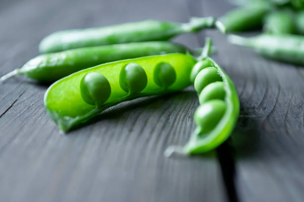 green pea beans in a pod on a wooden table. green peas with open pod. beans in a pod. - green pea pea pod salad legume imagens e fotografias de stock