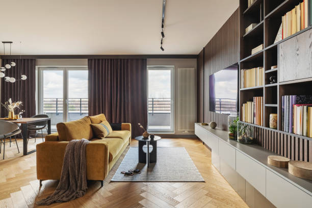 istock Creative and modern vintage living room interior design with yellow sofa and coffee table on grey carpet. Lamella wall with tv, bookcase and chest of drawers . Herringbone parquet., Brown curtain in windows. Template. 1405582066