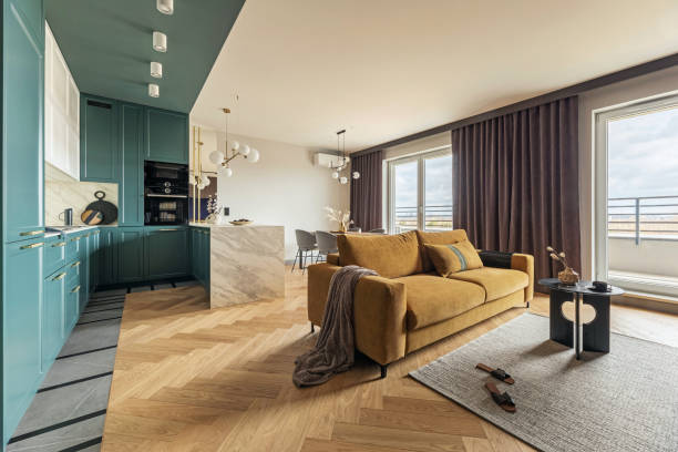 Creative and modern vintage open space interior design with yellow sofa and turquoise kitchen with a marble island. Grey carpet on the herringbone parquet with coffee table, brown curtain in windows. Template.