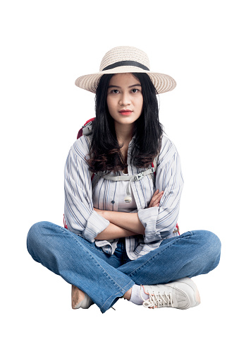Asian woman with hat and backpack sitting with crossed arms isolated over white background