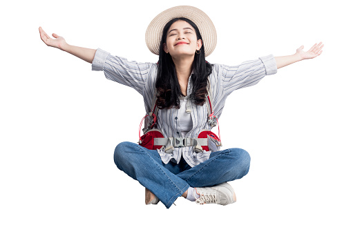 Asian woman with hat and backpack sitting with open arms isolated over white background