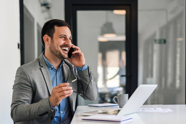 istock Cheerful entrepreneur talking on cellphone while working on laptop at office 1405587995