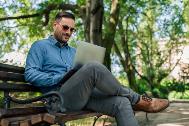 istock Confident businessman using laptop while sitting on bench at park 1405588062
