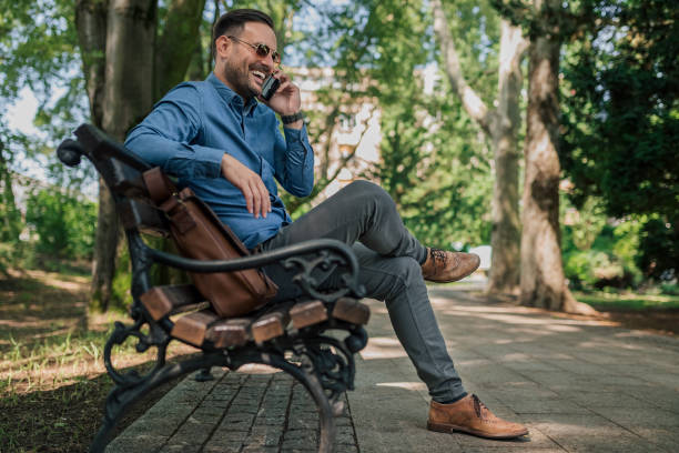 istock Smiling young entrepreneur talking on smart phone while sitting on park bench 1405588068